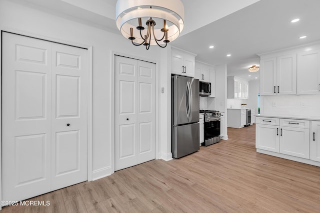 kitchen featuring appliances with stainless steel finishes, light wood finished floors, beverage cooler, a chandelier, and white cabinets