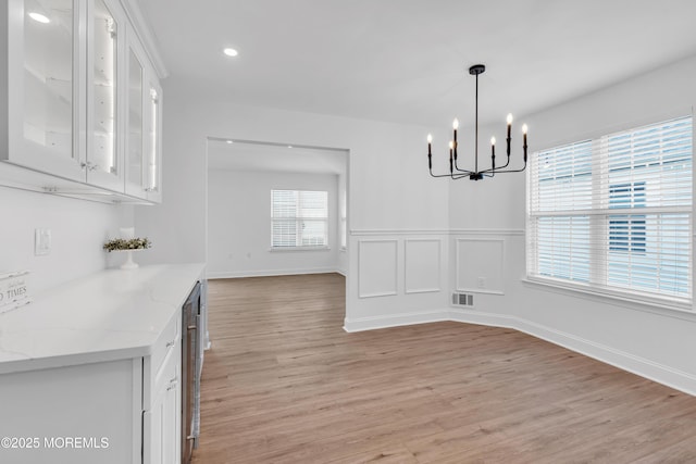 unfurnished dining area with a chandelier, light wood-style flooring, recessed lighting, and baseboards