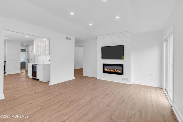 unfurnished living room with beverage cooler, light wood-style floors, recessed lighting, a fireplace, and baseboards