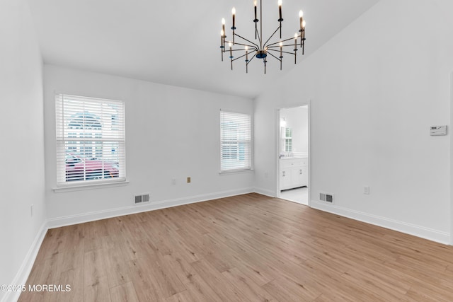 spare room with plenty of natural light, light wood-type flooring, a chandelier, and high vaulted ceiling
