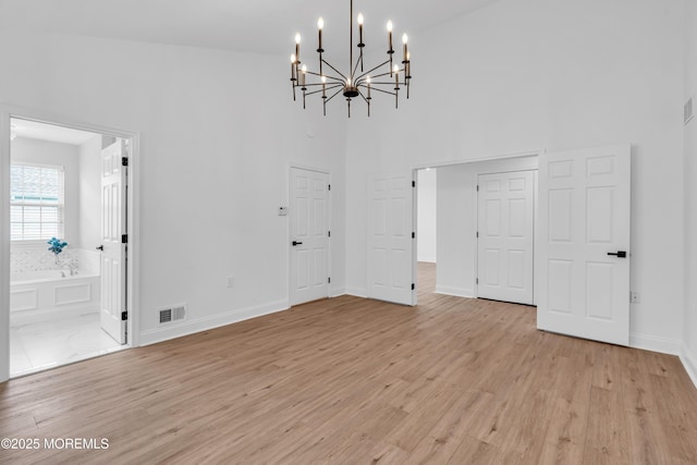 unfurnished dining area with a chandelier, a towering ceiling, light wood-style flooring, and baseboards