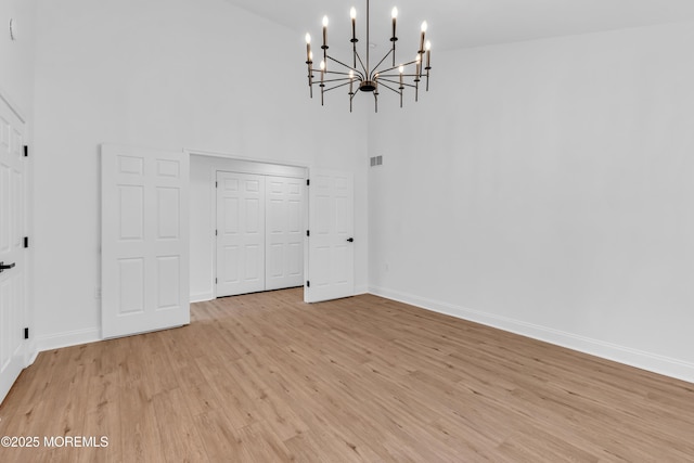 unfurnished dining area featuring a high ceiling, a chandelier, light wood-type flooring, and baseboards