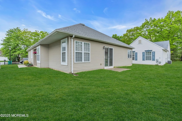 rear view of house with a yard, cooling unit, and a shingled roof
