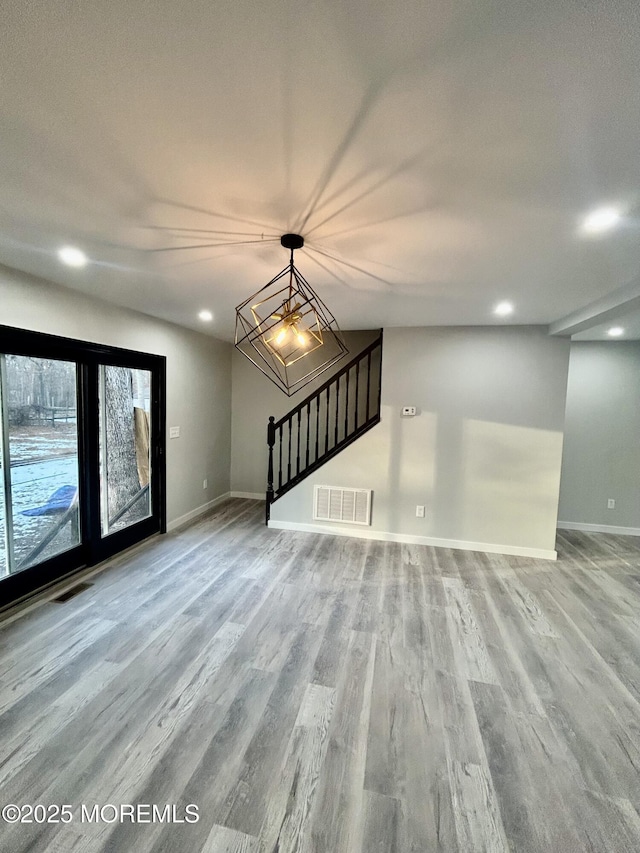 unfurnished living room with wood finished floors, baseboards, recessed lighting, stairway, and a chandelier