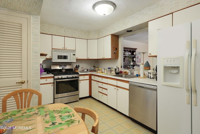 kitchen featuring appliances with stainless steel finishes, a sink, light countertops, light flooring, and a textured ceiling