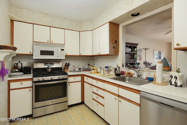 kitchen with stainless steel appliances, a sink, light countertops, light flooring, and a textured ceiling