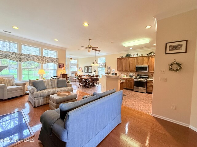 living area with crown molding, ceiling fan, recessed lighting, light wood-style flooring, and baseboards