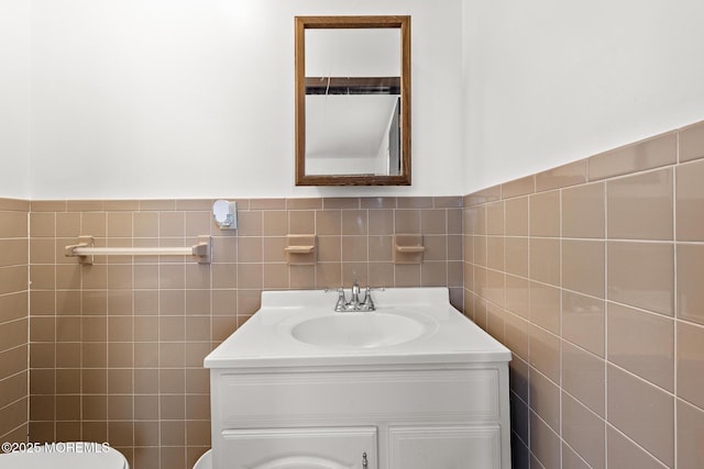 half bath featuring tile walls, toilet, vanity, and a wainscoted wall