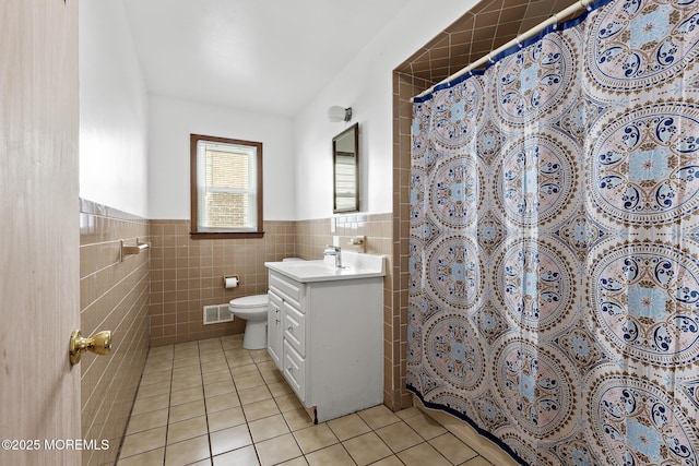 bathroom featuring toilet, tile patterned flooring, tile walls, wainscoting, and vanity
