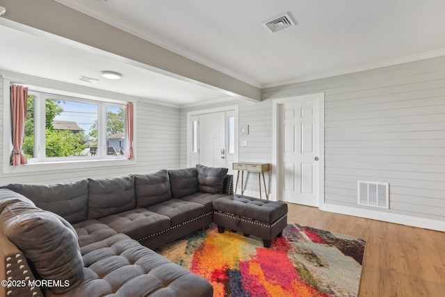 living area with wood finished floors, ornamental molding, baseboards, beam ceiling, and wood walls