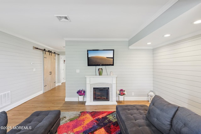 living area featuring a barn door, ornamental molding, wood walls, wood finished floors, and baseboards