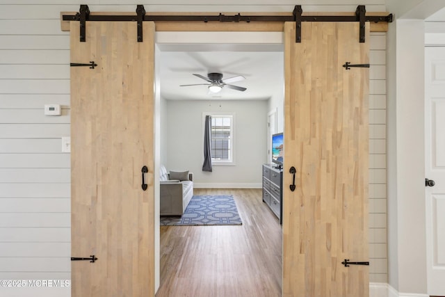living room with a barn door, wood finished floors, a ceiling fan, and baseboards