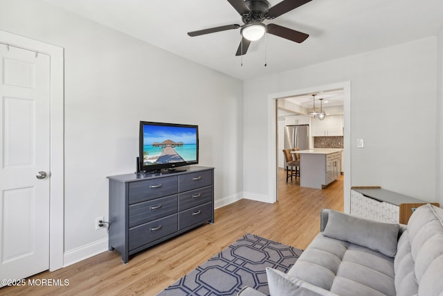 living room featuring light wood-style floors, baseboards, a ceiling fan, and a chandelier