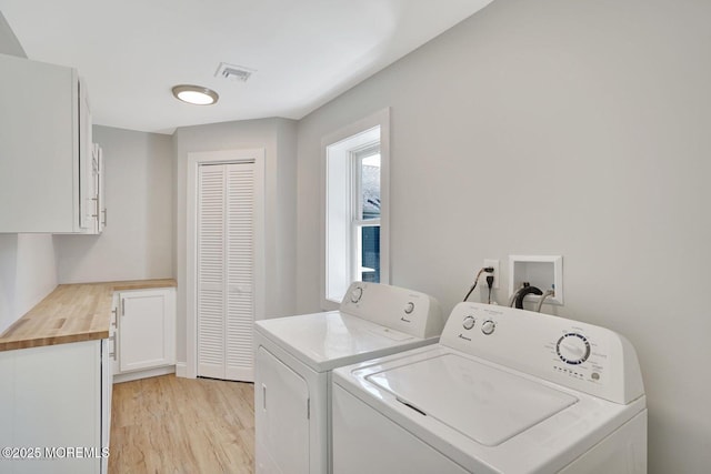 laundry room featuring washing machine and clothes dryer, cabinet space, and light wood-style flooring