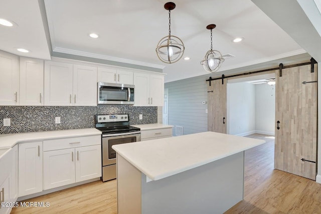 kitchen featuring appliances with stainless steel finishes, a barn door, crown molding, backsplash, and light wood finished floors