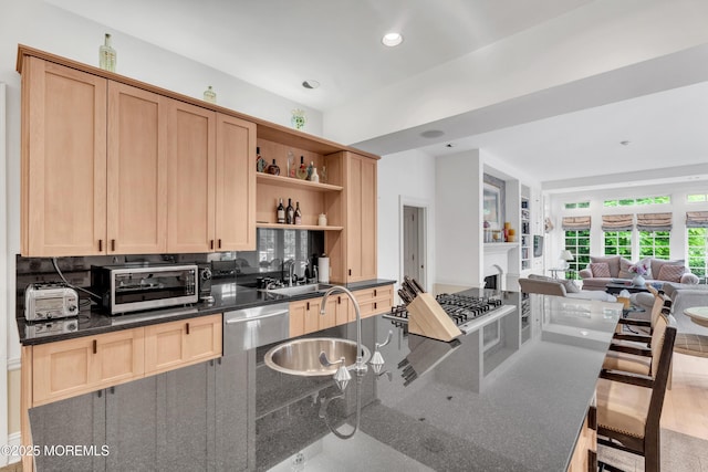 kitchen featuring appliances with stainless steel finishes, open floor plan, open shelves, a sink, and light brown cabinetry