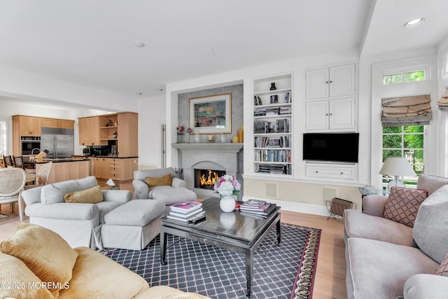 living area with light wood finished floors, a warm lit fireplace, built in features, and recessed lighting