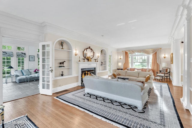 living room with ornamental molding, built in shelves, a glass covered fireplace, hardwood / wood-style floors, and baseboards