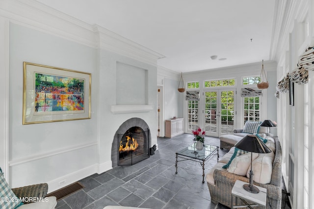 living area featuring french doors, a lit fireplace, ornamental molding, baseboards, and dark stone finish floors