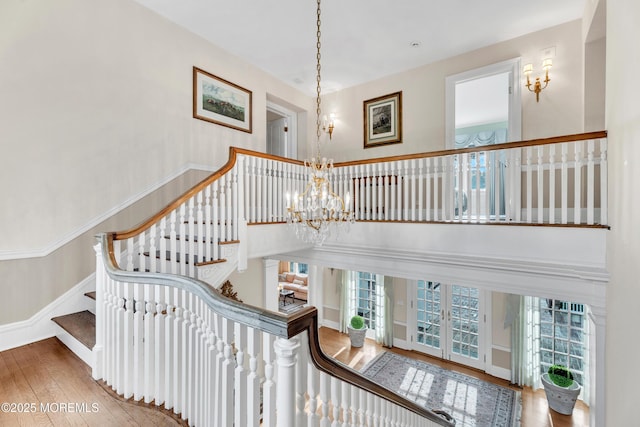 stairs featuring hardwood / wood-style flooring, french doors, a chandelier, baseboards, and a high ceiling