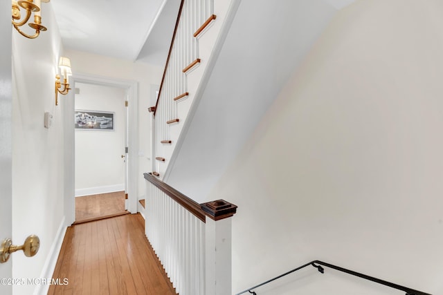 hallway with light wood-style flooring, stairway, and baseboards