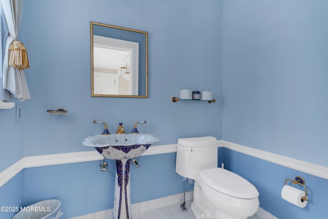half bathroom with toilet, tile patterned floors, and baseboards