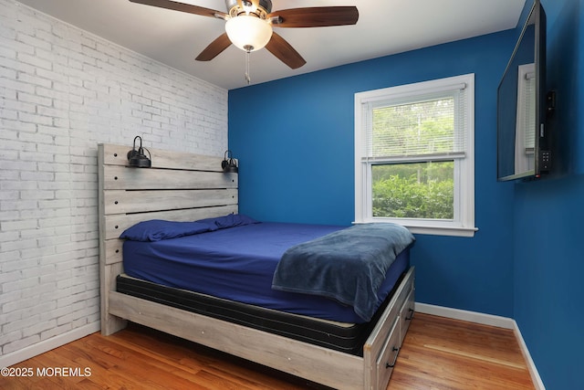 bedroom with brick wall, wood finished floors, baseboards, and ceiling fan