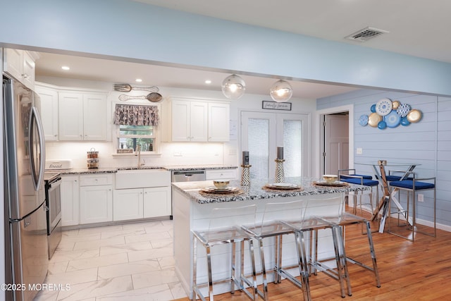 kitchen with freestanding refrigerator, a sink, light stone counters, a breakfast bar, and white cabinetry