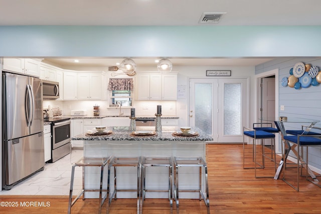 kitchen with appliances with stainless steel finishes, a sink, a kitchen breakfast bar, light stone counters, and white cabinets