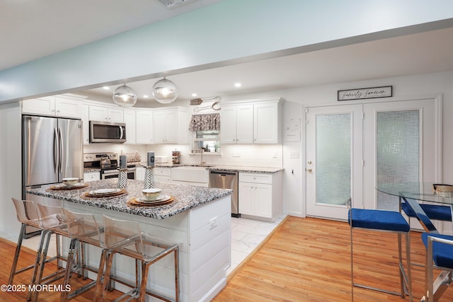 kitchen with appliances with stainless steel finishes, a sink, white cabinetry, light stone countertops, and a breakfast bar area