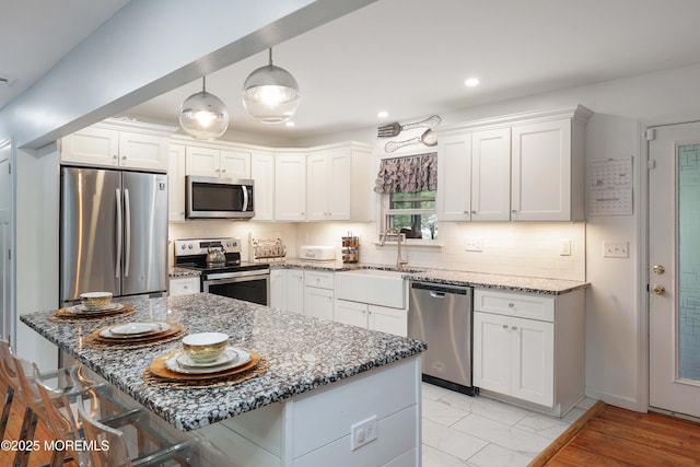 kitchen featuring stainless steel appliances, a sink, light stone countertops, white cabinets, and recessed lighting