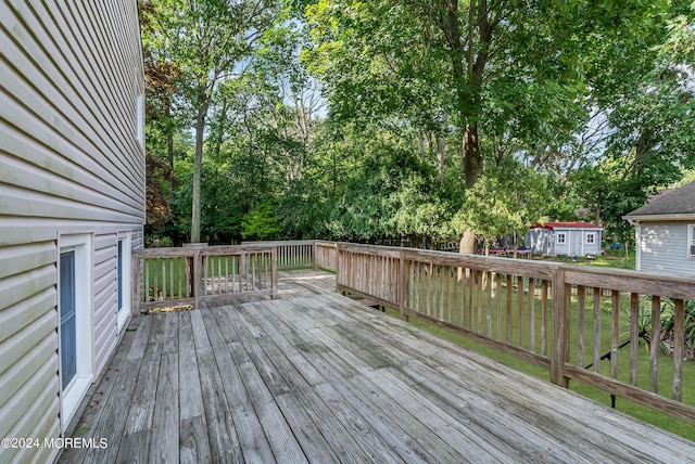 wooden terrace featuring an outdoor structure, view of wooded area, and a storage unit