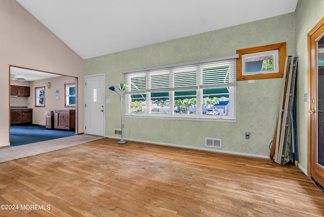 foyer featuring light wood finished floors, healthy amount of natural light, high vaulted ceiling, and baseboards