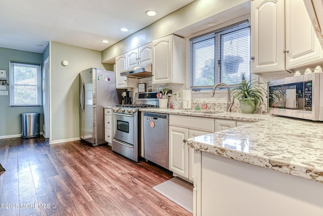 kitchen featuring stainless steel appliances, a sink, under cabinet range hood, dark wood-style flooring, and baseboards
