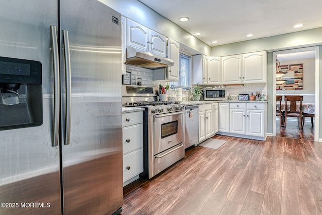kitchen featuring stainless steel appliances, under cabinet range hood, white cabinetry, light wood finished floors, and recessed lighting