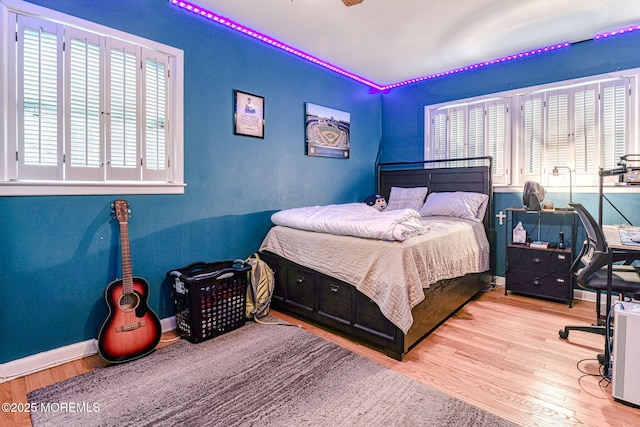bedroom with multiple windows, wood finished floors, and baseboards