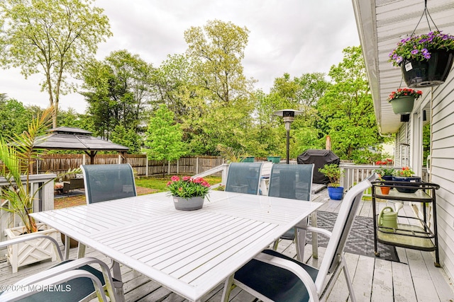wooden terrace with outdoor dining area, a fenced backyard, and a gazebo