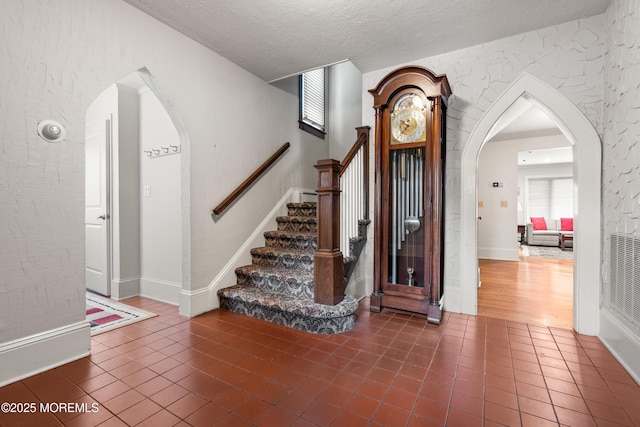 567 Deal Pkwy, Allenhurst, NJ 07711 - stairs featuring tile patterned flooring, a textured ceiling, arched walkways, a textured wall, and baseboards
