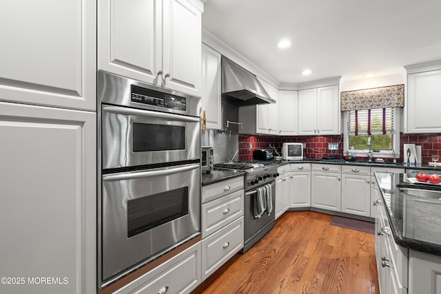 567 Deal Pkwy, Allenhurst, NJ 07711 - kitchen featuring stainless steel appliances, wall chimney exhaust hood, white cabinets, light wood-style flooring, and decorative backsplash