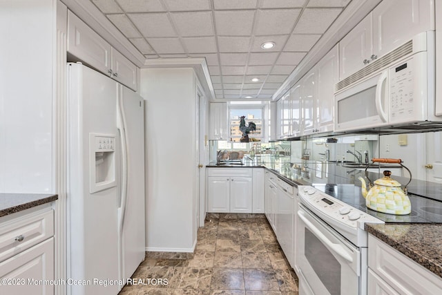 kitchen with white appliances, white cabinets, dark stone countertops, a paneled ceiling, and baseboards