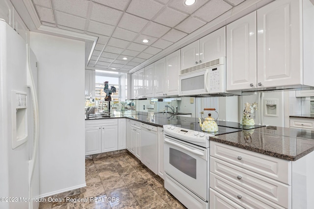kitchen featuring white appliances, white cabinetry, a sink, dark stone counters, and baseboards