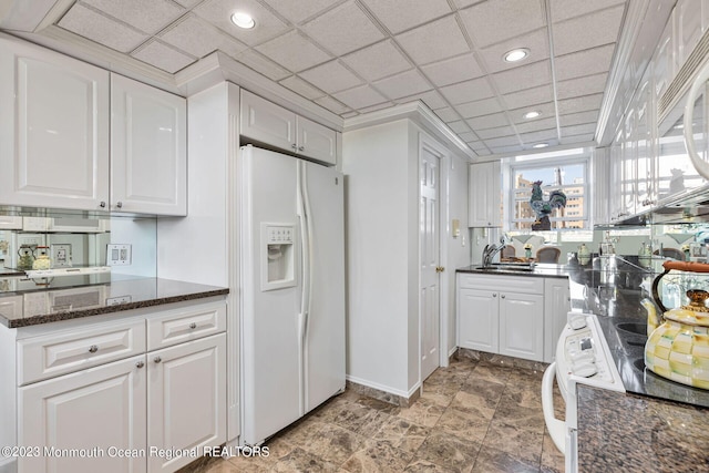 kitchen with white appliances, white cabinetry, recessed lighting, dark stone counters, and a sink