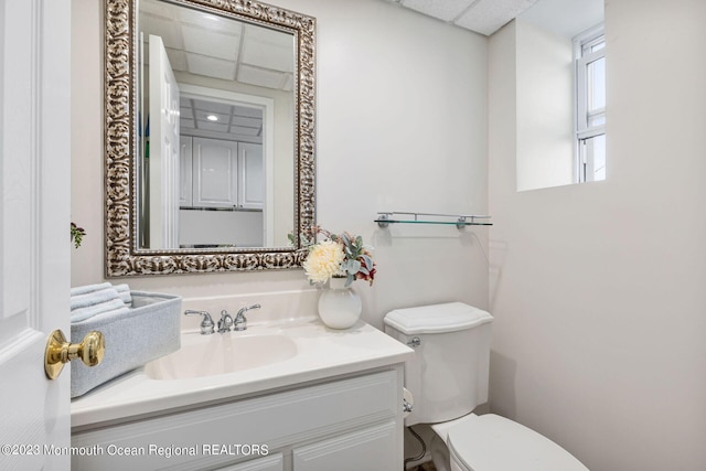 half bathroom featuring toilet, vanity, and a paneled ceiling