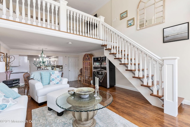 living room with stairway, wood finished floors, a high ceiling, crown molding, and a chandelier