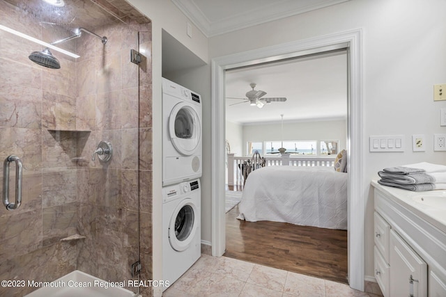 ensuite bathroom with estacked washer and dryer, a ceiling fan, ornamental molding, and a stall shower