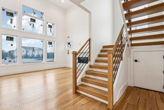 stairway with a high ceiling, wood finished floors, and baseboards