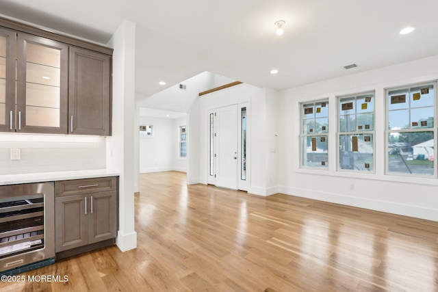 kitchen featuring beverage cooler, light countertops, backsplash, baseboards, and light wood-type flooring
