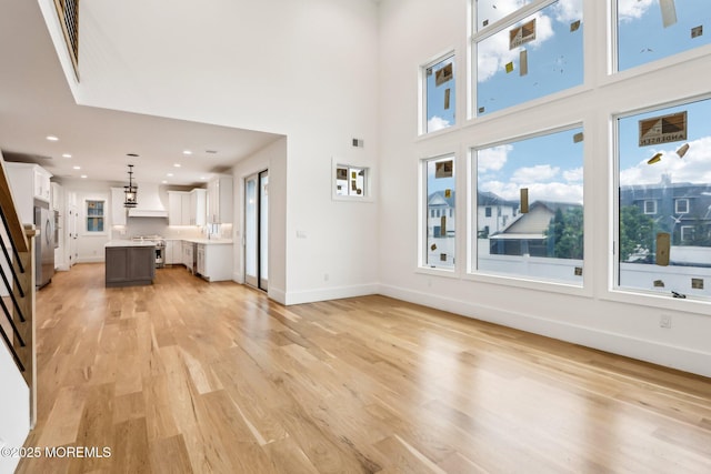 unfurnished living room featuring light wood-type flooring, healthy amount of natural light, recessed lighting, baseboards, and a high ceiling