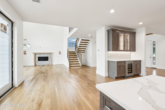 kitchen with beverage cooler, open floor plan, light wood-style flooring, a fireplace, and dark brown cabinets