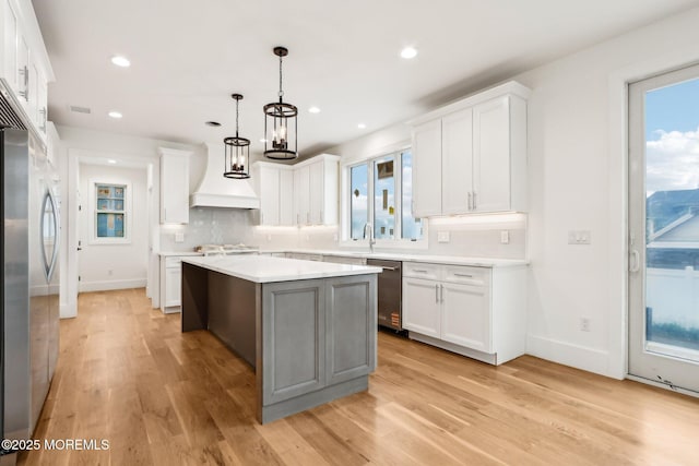 kitchen featuring custom exhaust hood, stainless steel appliances, light countertops, a kitchen island, and baseboards